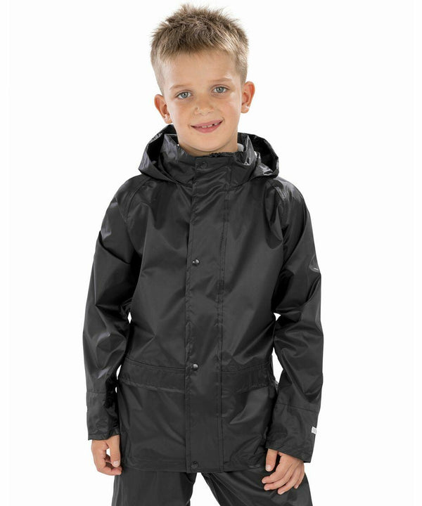 A young boy stands smiling, wearing a black Result R227J rain jacket with a hood, against a plain white background.
