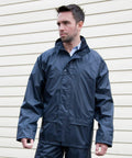 A man wearing a dark blue Result R227X rain jacket stands in front of a beige wall.