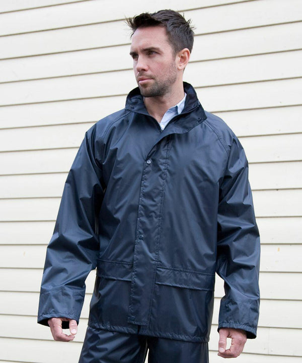 A man wearing a dark blue Result R227X rain jacket stands in front of a beige wall.