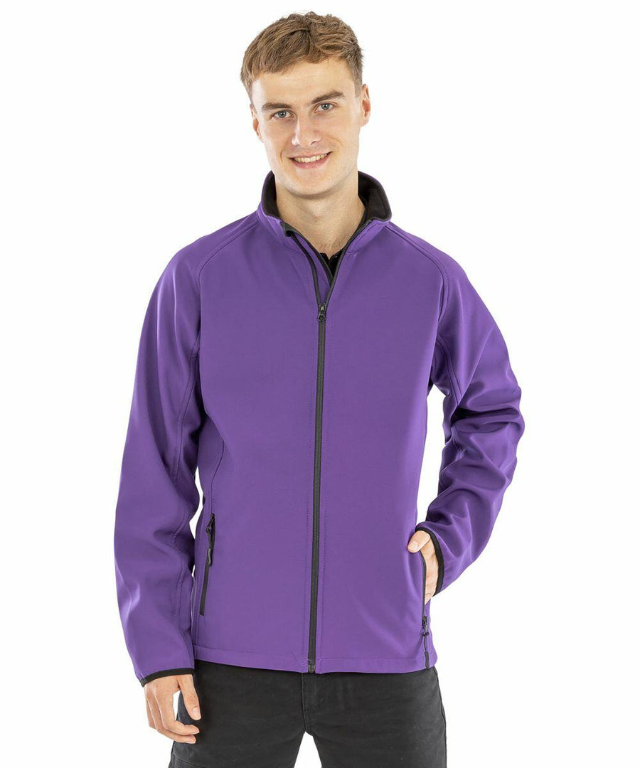 A person is standing and smiling, wearing a purple Result R231M jacket and black pants. One hand is in their pocket, and the other arm rests at their side.