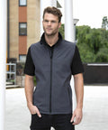 A man stands outdoors wearing a grey zip-up vest (Result R232M) over a black shirt and black pants, with a building and greenery in the background.