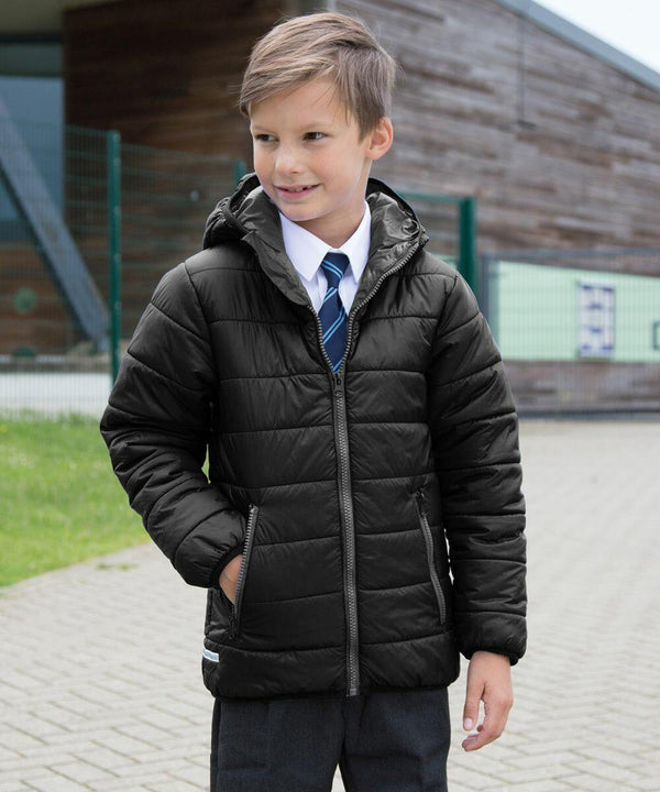A boy with brown hair, wearing a black puffer jacket, blue tie, and grey pants, stands outside near a modern building in a Result R233J.