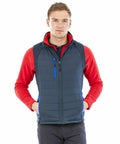 Young man wearing a red long-sleeve shirt and a dark blue Result Genuine Recycled R238X stands facing the camera with his hands in the pockets of his vest.