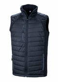 The R238X by Result Genuine Recycled is a black quilted sleeveless vest featuring a front zipper. It includes a high collar, two side pockets, and one zippered chest pocket. The vest has a textured design and looks lightweight, making it ideal for layering.