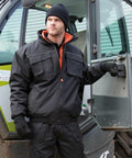 A person wearing a Result R300X jacket, gloves, and beanie stands next to an open door of a vehicle, with part of a building visible in the background.