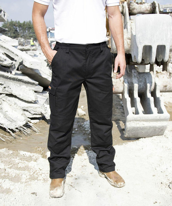 A person wearing black cargo pants and brown Result R303X work boots stands near heavy construction machinery on a muddy, debris-filled construction site.