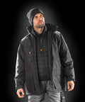 A man wearing a black beanie, multiple layers of black jackets including the Result R305X, and gray pants stands against a dark background.