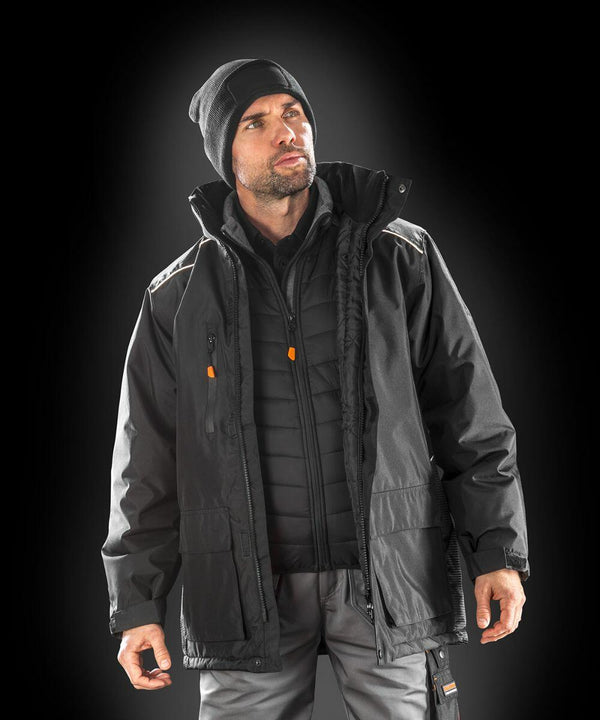 A man wearing a black beanie, multiple layers of black jackets including the Result R305X, and gray pants stands against a dark background.