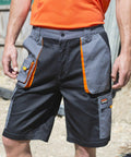 A person wearing dark gray and black Result R319X work shorts with orange accents and multiple pockets. They are also wearing an orange shirt.