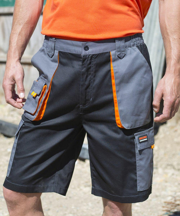 A person wearing dark gray and black Result R319X work shorts with orange accents and multiple pockets. They are also wearing an orange shirt.