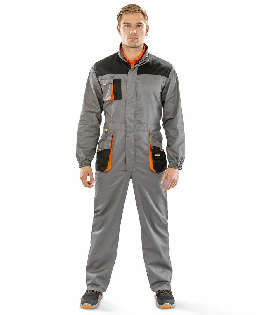 A person in a Result R321X coverall with orange accents stands facing forward. The coverall has multiple pockets and the individual is wearing grey sneakers with orange details.