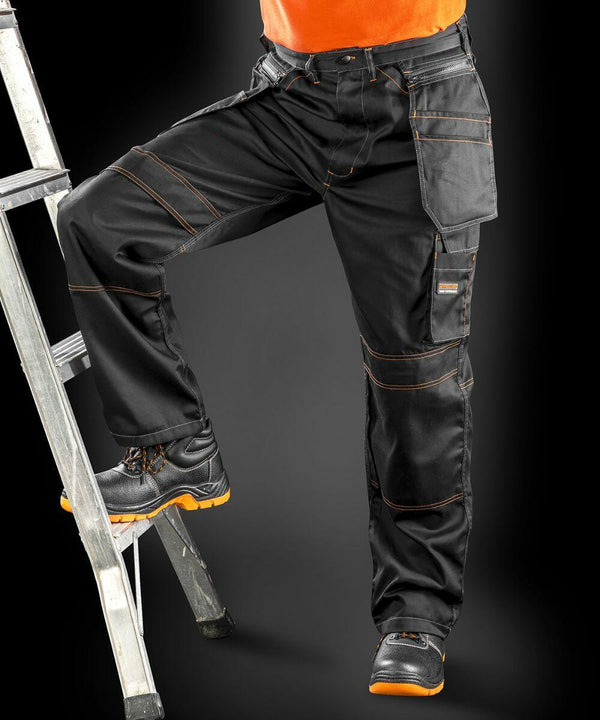 A person wearing Result R323X black work pants and boots with orange accents stands on a ladder.