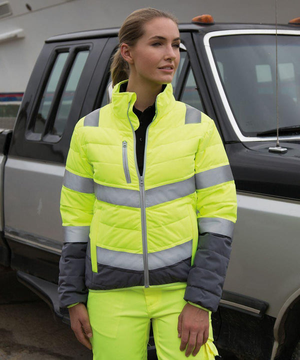 Person wearing a high-visibility yellow and gray Result R325F jacket and pants, standing beside a pickup truck.