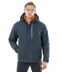 A man with glasses is wearing a dark blue hooded jacket with front pockets and an orange inner lining, posing with one hand in his pocket. The jacket is the R326X from Result.