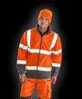 A person wearing a Result R329X orange high-visibility jacket and beanie stands against a black background.