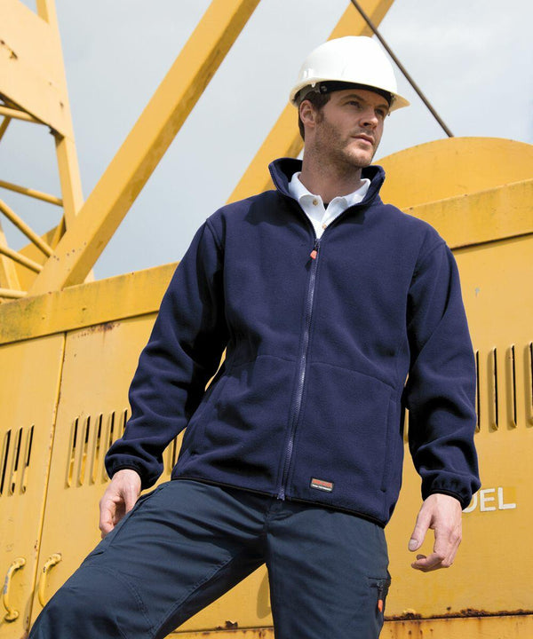 Man wearing a blue Result R330X jacket and white hard hat stands in front of a yellow industrial crane.
