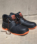 A pair of black and orange R340X work boots by Result with "WORLD GUARD" label, positioned on a concrete surface. One boot has its laces untied.