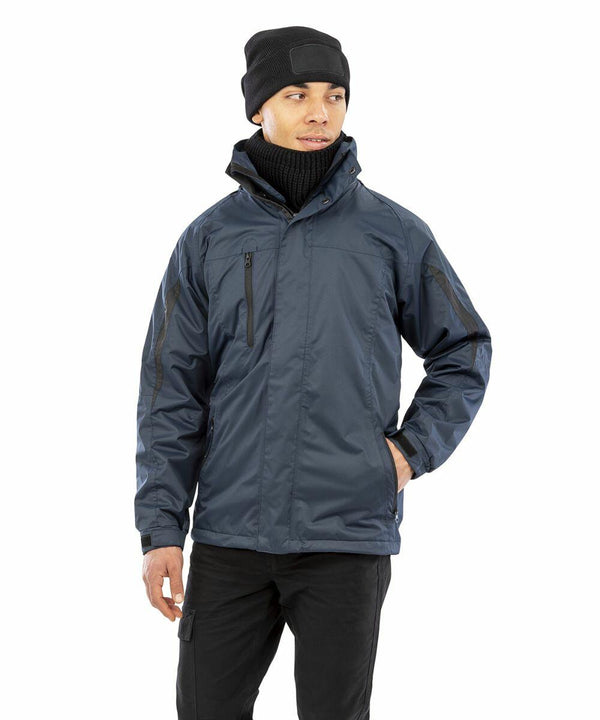 Person wearing a dark blue Result R400M jacket, black beanie, and a black scarf, standing with one hand in a pocket and looking to the side.