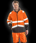 A man wearing a Result R450X high-visibility work jacket and matching pants stands against a dark background.
