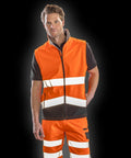 Person wearing a Result R451X orange high-visibility vest and pants with reflective stripes, standing against a black background.