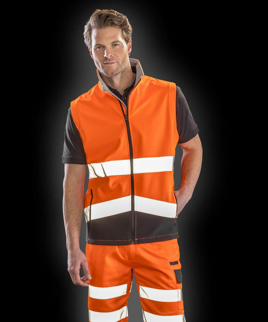Person wearing a Result R451X orange high-visibility vest and pants with reflective stripes, standing against a black background.