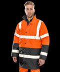 Person wearing a Result R452X high-visibility jacket with reflective white stripes, black lower sections, and orange trousers, stands against a black background.