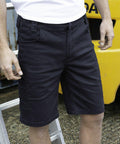 Person wearing black cargo shorts and a white Result R471X shirt stands near a yellow forklift and a metal ladder.