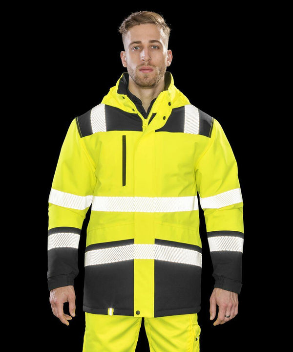 A man wearing a bright yellow and black high-visibility jacket with reflective stripes, the Result R475X, stands in front of a black background.