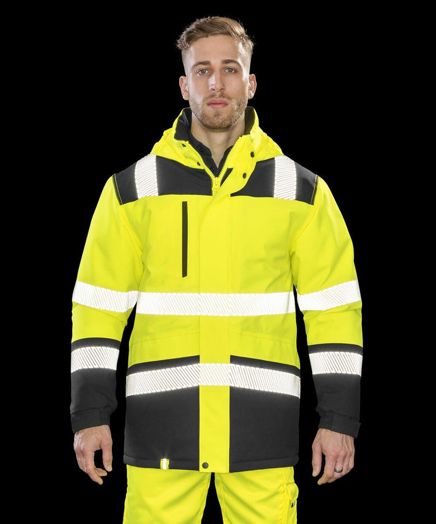 A man wearing a bright yellow and black high-visibility jacket with reflective stripes, the Result R475X, stands in front of a black background.