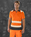 A man wearing an orange high-visibility R501X work polo and pants from Result stands against a grey background.
