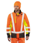 A person models the Result Recycled 3-layer printable 3-tone safety softshell, featuring an orange high-visibility jacket with reflective strips, yellow panels, black accents, a matching beanie, and orange trousers.