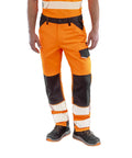 A person wearing Result Safeguard Safe-Guard recycled dynamic stretch safety trousers in orange and black with reflective stripes, a belt, black shoes with orange soles, and a matching high-visibility shirt, shown from shoulders down.