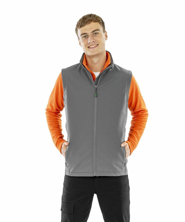 A young man wearing an orange long-sleeve shirt and a grey Result R902M smiles with his hands in his vest pockets.