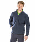 A man wearing a dark blue Result R903X and green shirt smiles at the camera with one hand in his pocket.