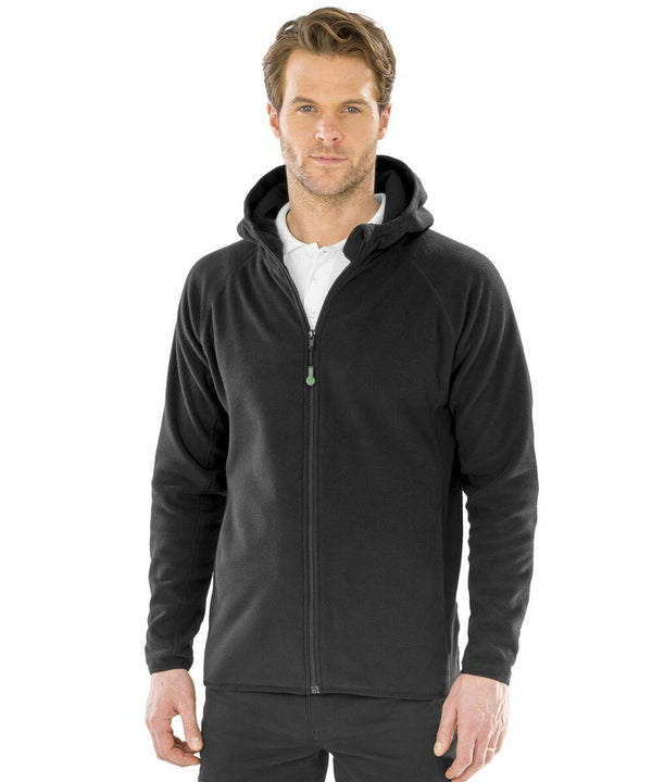 A man is wearing a black Result Genuine Recycled R906X hoodie over a white polo shirt. He has short, light brown hair and is standing against a plain white background.