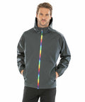 A man wearing a dark grey Result Genuine Recycled R908X with a colorful rainbow zipper stands with his hands in his pockets.
