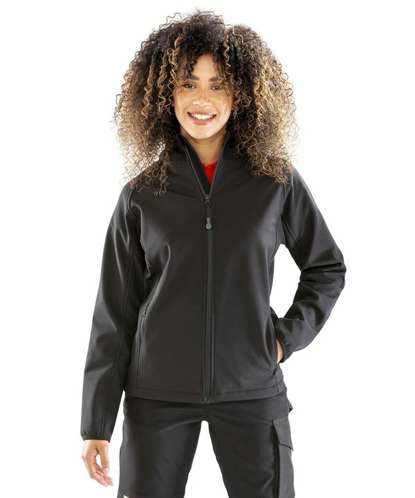 Person wearing a black Result Genuine Recycled R911F zip-up jacket and dark pants, standing with hands in pockets against a plain white background.
