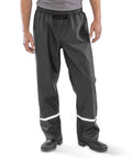 A person shown from the waist down is wearing Result Recycled Prism PU waterproof trousers with reflective bands, black boots, and a grey shirt.