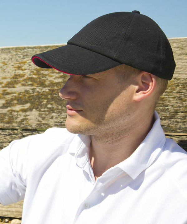 A person wearing a black RC24P Result baseball cap and white polo shirt is sitting outdoors, looking into the distance, with a wooden background visible.