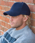 A person wearing a navy RC25X by Result and a gray sweater leans against a brick wall.
