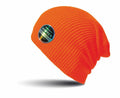 A beanie from Result Winter Essentials, the RC31X model, features an orange knit design with a small, round patch showcasing a colorful logo on the side. It is shown against a white background with subtle shadowing beneath it.