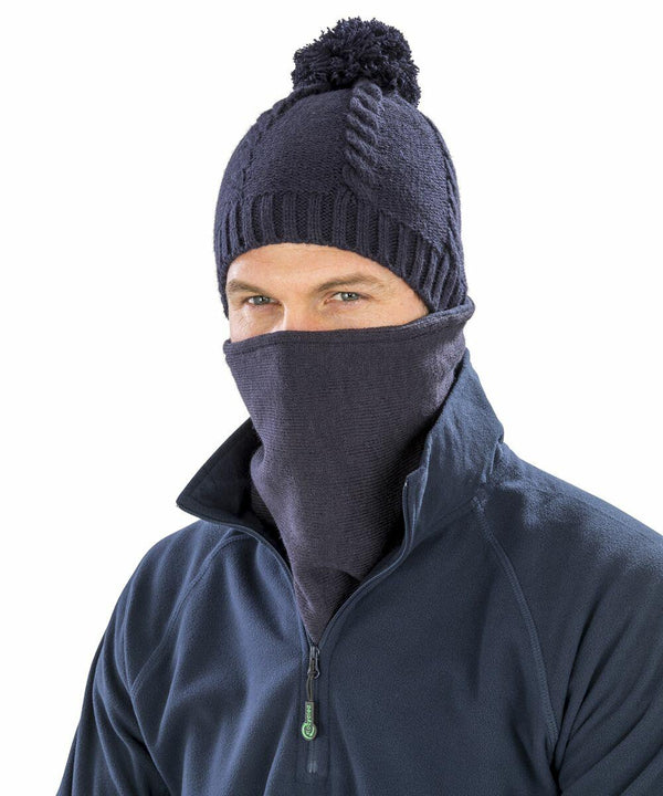 A person wearing a navy blue beanie with a pom-pom and a matching navy blue neck gaiter, covering their nose and mouth. The person is also dressed in a dark blue Result RC353 jacket.