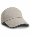 The RC38X beige baseball cap by Result Headwear, featuring a curved brim with a dark contrasting trim, is displayed at an angle against a plain white background.
