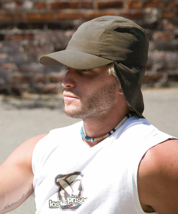 A person with light hair wearing a khaki RC69X by Result, sleeveless white shirt, and necklace is standing outdoors.