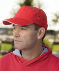 A man wearing a Result RC72X red cap and a matching hoodie looks into the distance outdoors.