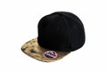 Result Headwear's RC87X is a black snapback hat featuring a gold marbled brim, complete with a round sticker on the brim.