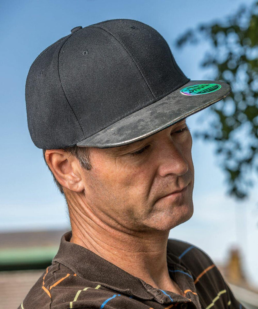 A man wearing a black **Result RC87X** and a brown striped shirt looks downward outdoors against a backdrop of a clear sky and foliage.