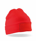 The RC934, a vibrant red knit beanie from Result Genuine Recycled, features a folded brim and a rectangular patch on the front. It is displayed against a plain white background.