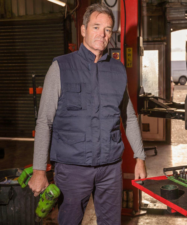 A man wearing a padded vest and long-sleeve shirt holds a green Result RE94A in a workshop with equipment and machinery visible in the background.