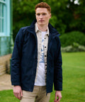 Man with short red hair wearing a Regatta RG051 jacket over a white shirt stands outdoors on a grassy area with trees and a building in the background.